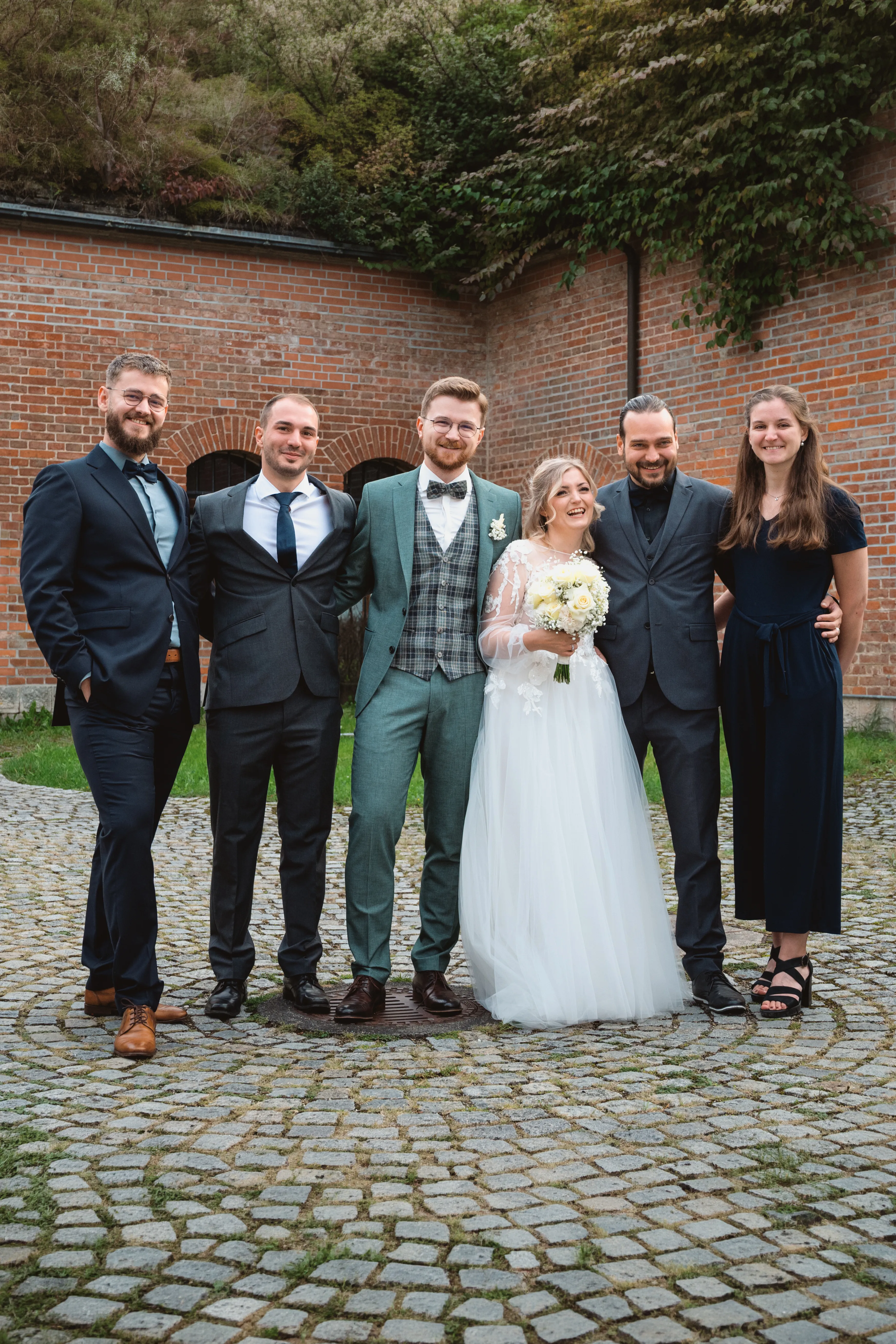 Tamara und Kevin mit vier Gästen vor einer Backsteinwand im Innenhof.