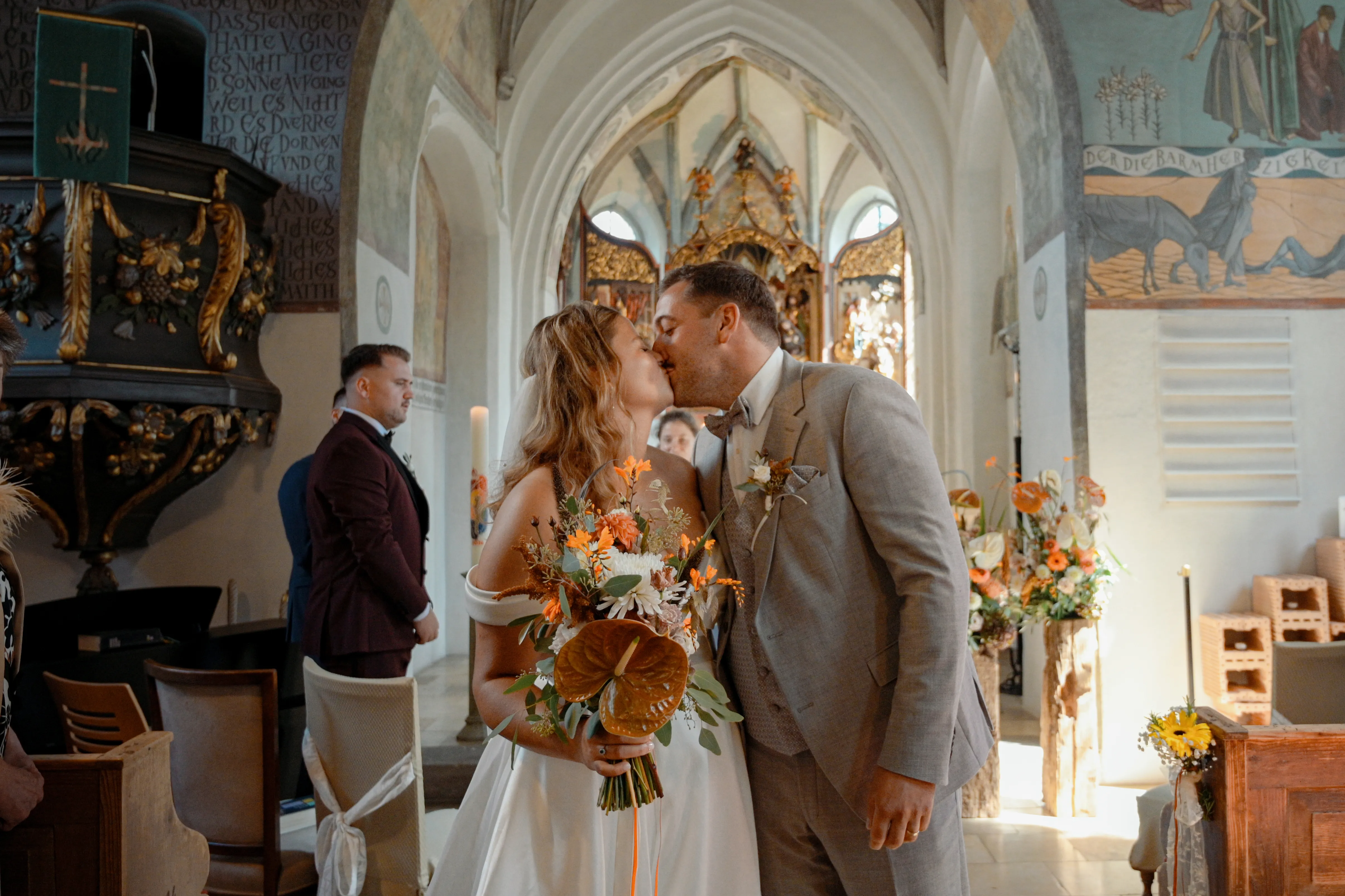 Lisa und Martin küssen sich in der Kirche in Reutti; Lisa hält ihren Brautstrauß.