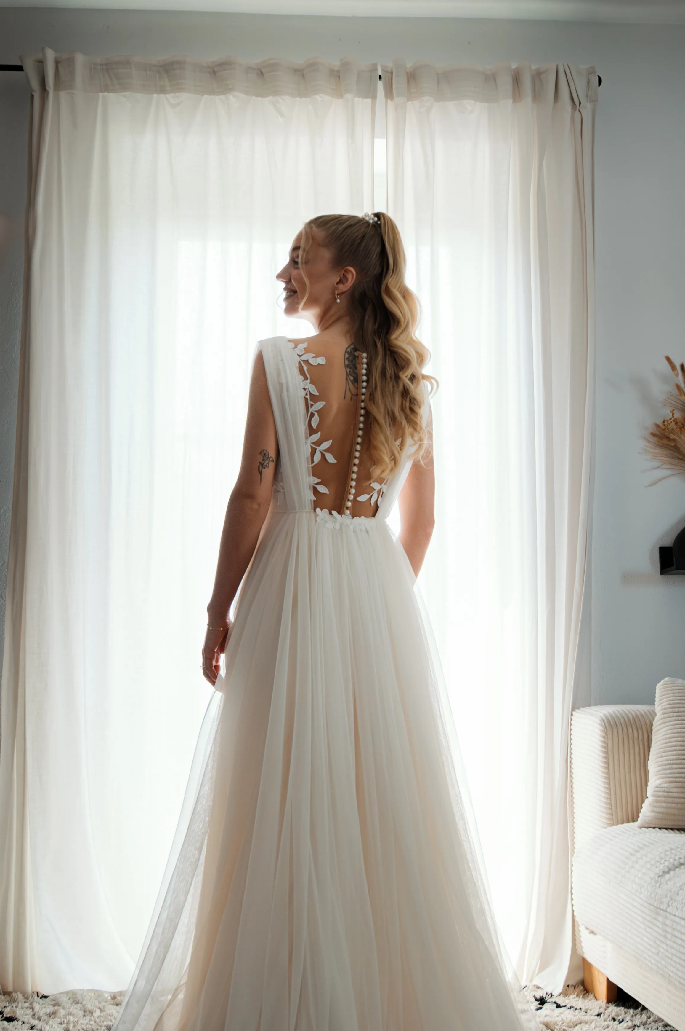 Eine Braut steht mit dem Rücken zum hellen Fenster.