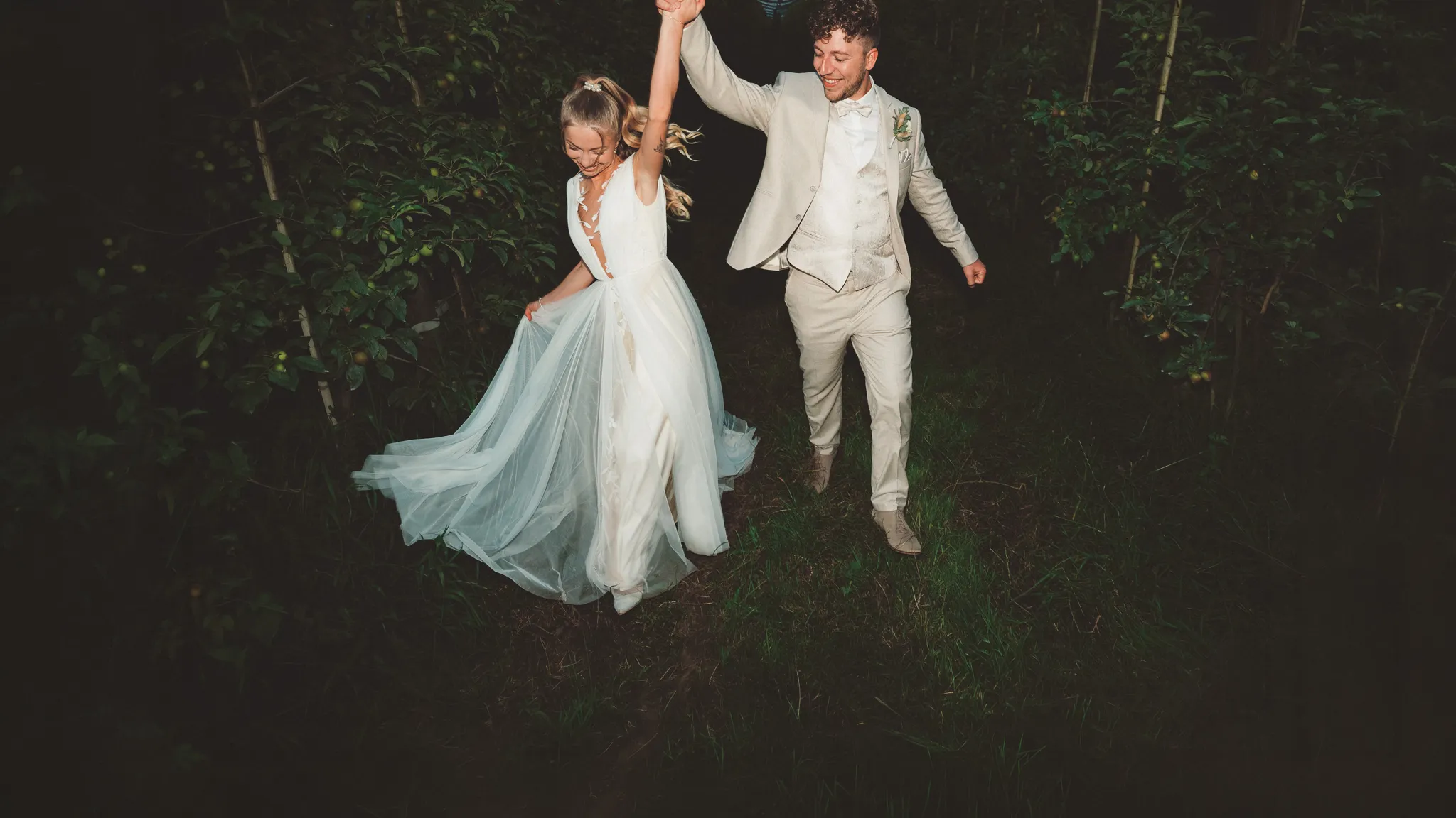 Franziska und Daniel tanzen Hand in Hand zwischen den Bäumen bei Nacht.