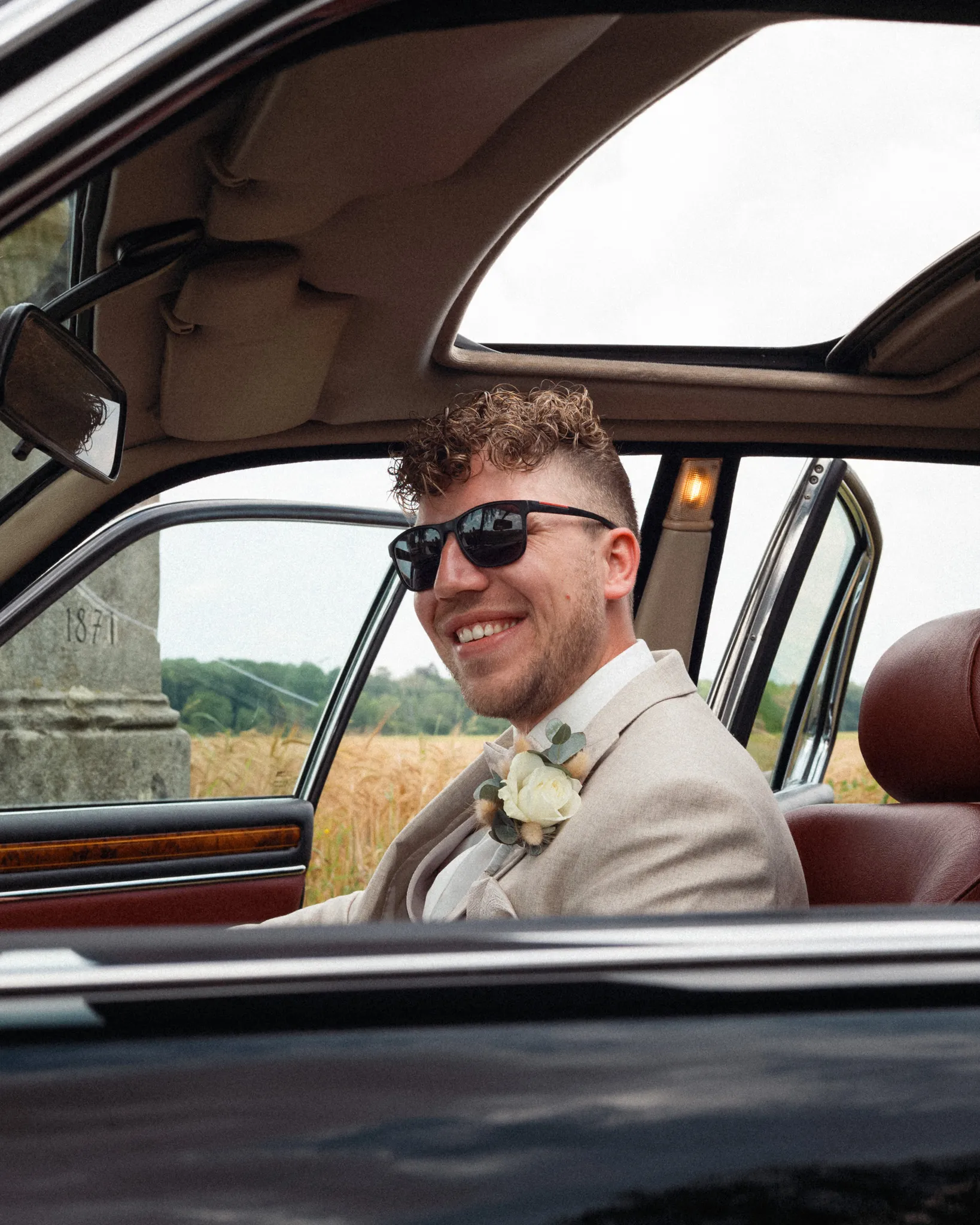 Daniel sitzt mit Sonnenbrille im geöffneten Hochzeitsauto.