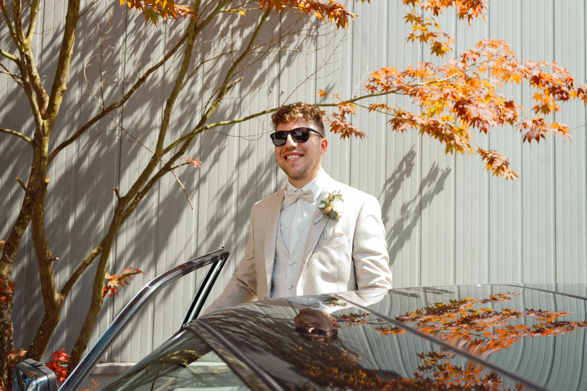 Daniel lehnt lächelnd am Hochzeitsauto.