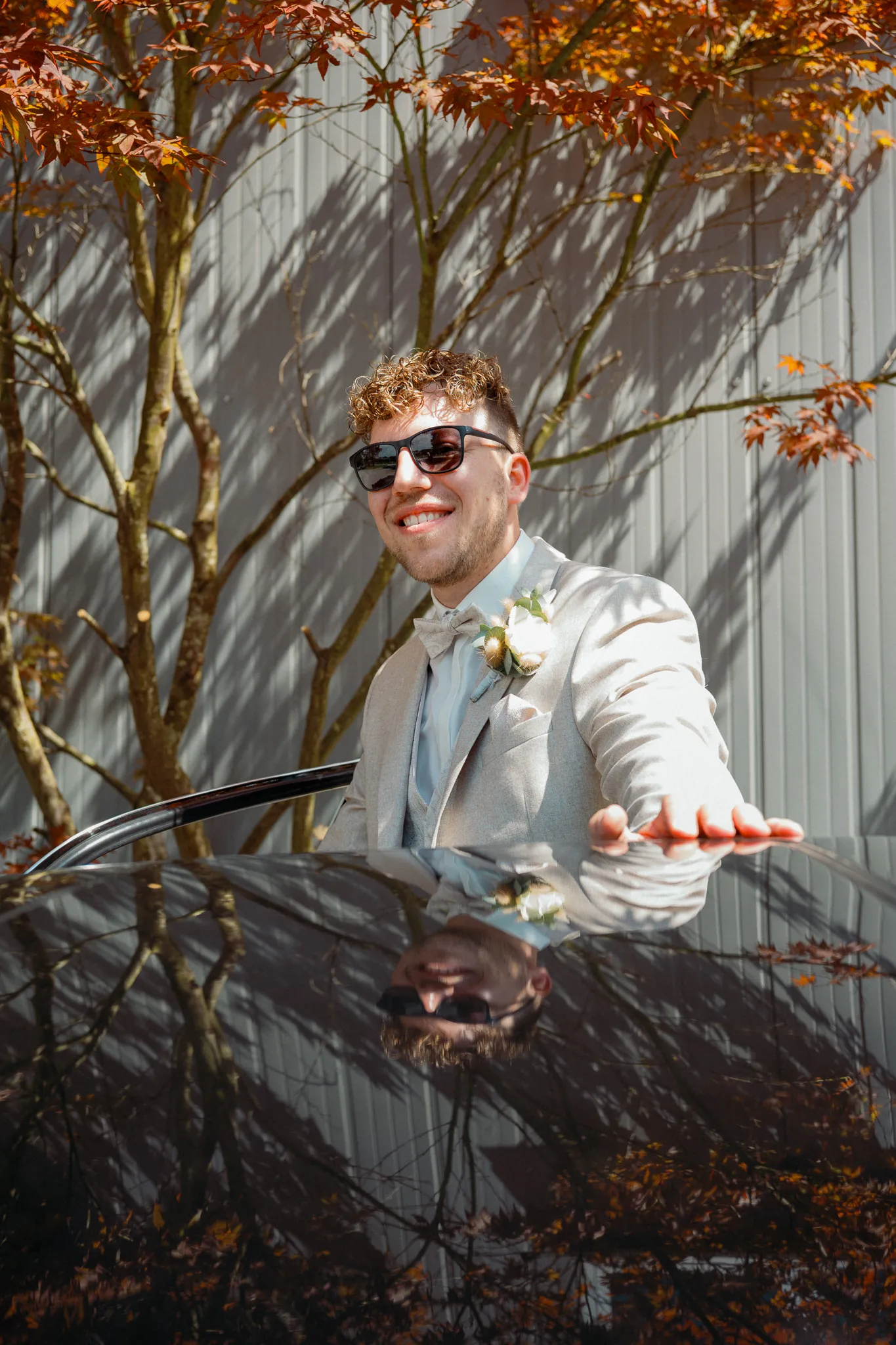 Daniel steht mit Sonnenbrille neben einem Baum mit roten Blättern.