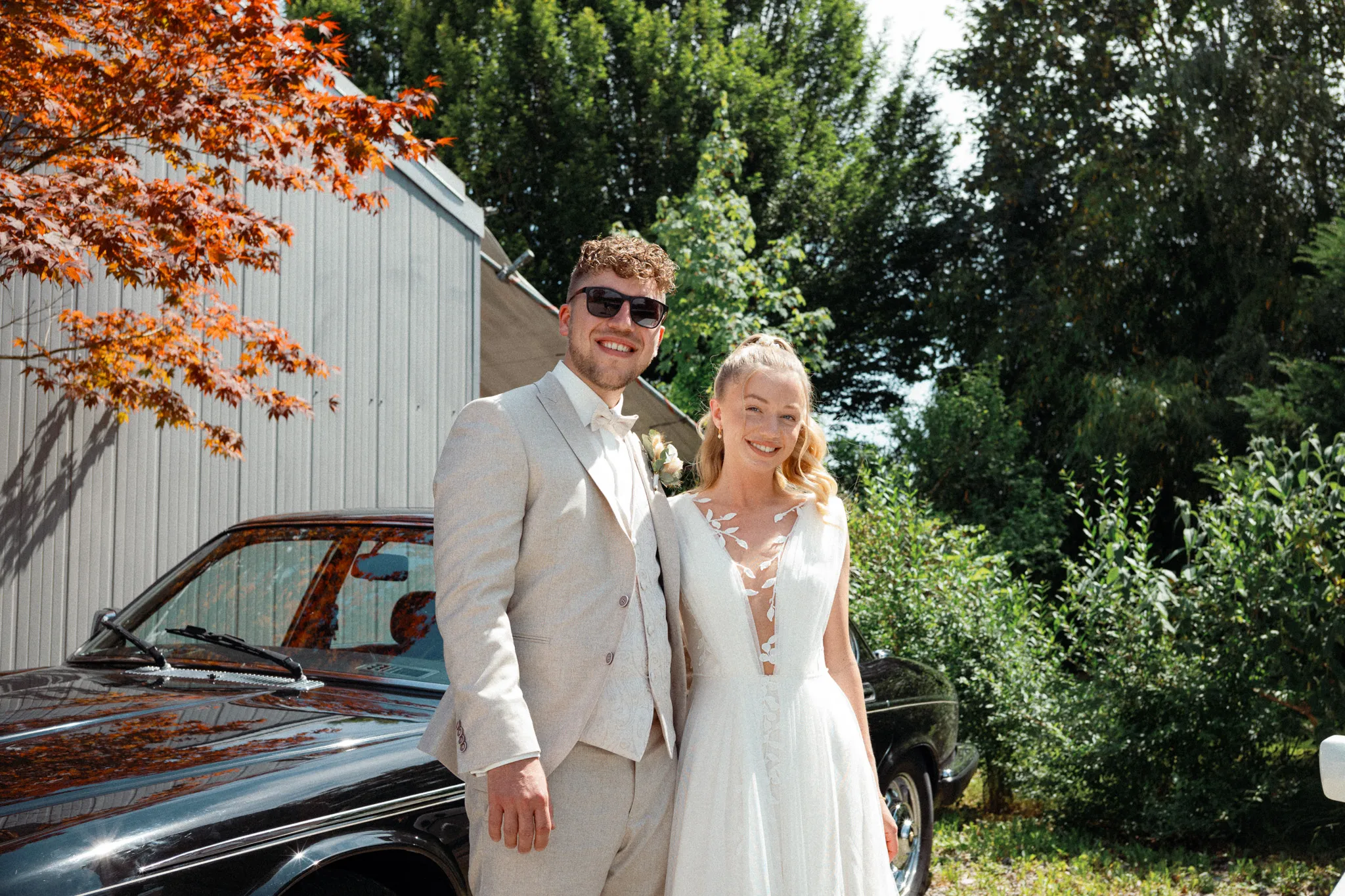 Franziska und Daniel stehen gemeinsam vor dem Hochzeitsauto.