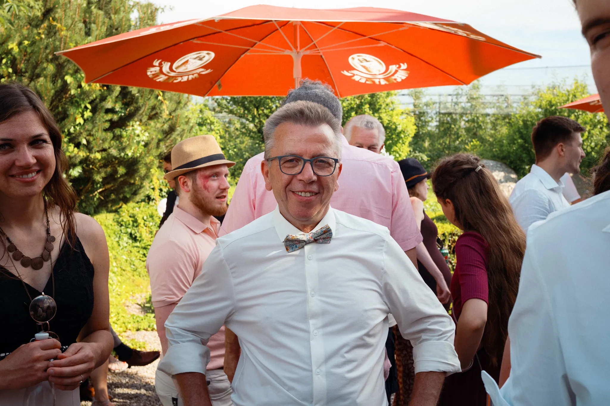 Ein Hochzeitsgast lächelt im Garten in die Kamera.
