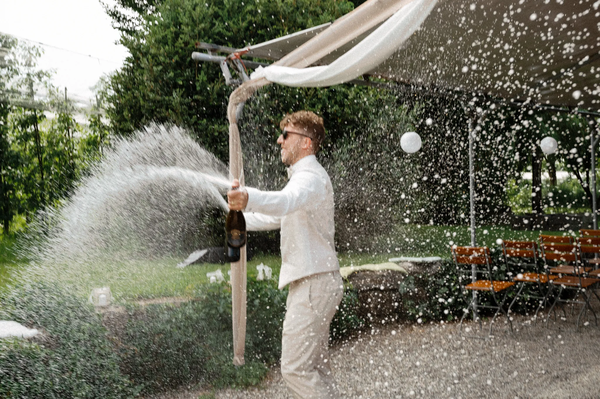 Ein Gast öffnet eine sprudelnde Flasche im Garten.