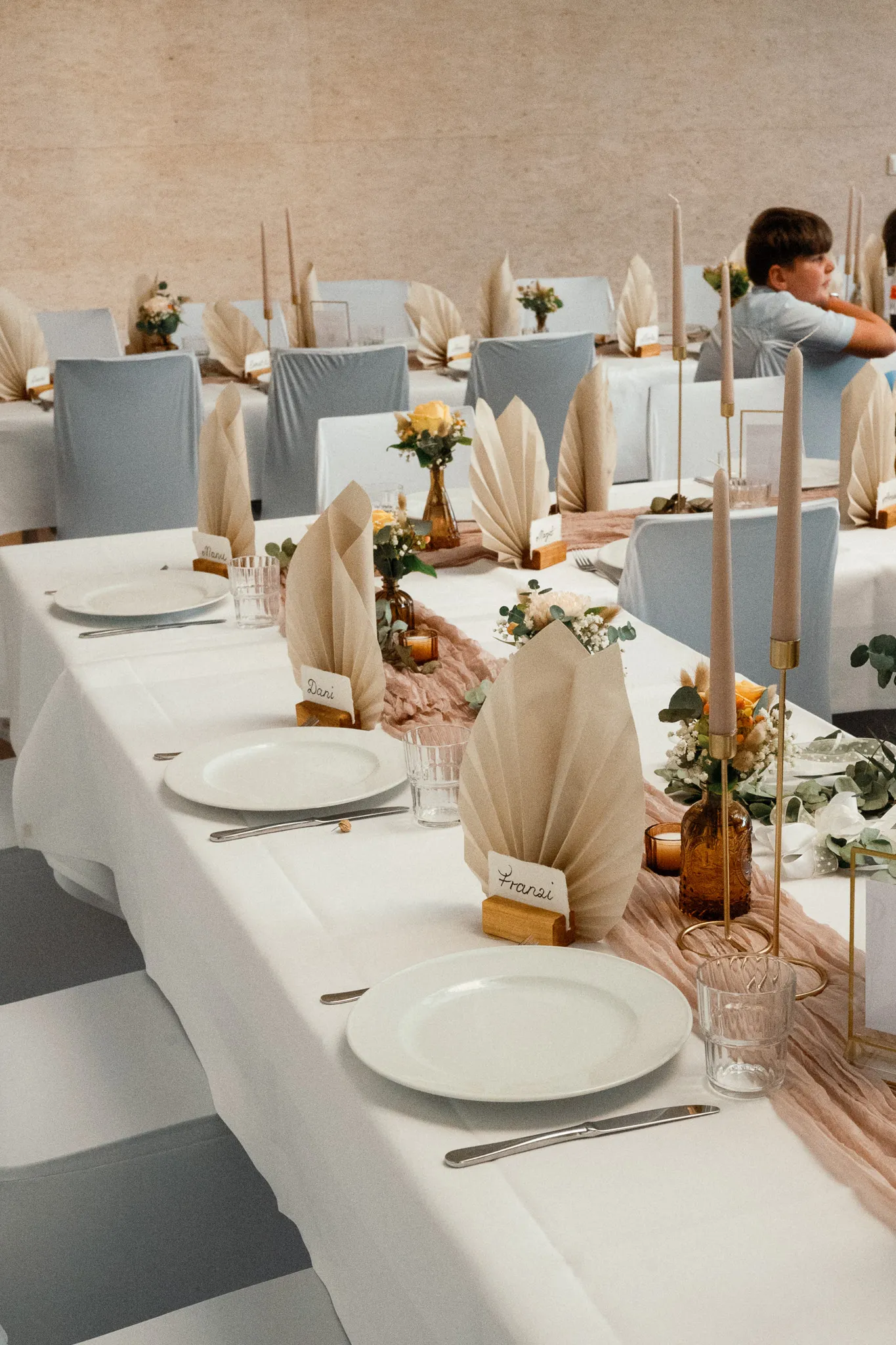 Kerzen und Blumen stehen auf der gedeckten Hochzeitstafel.
