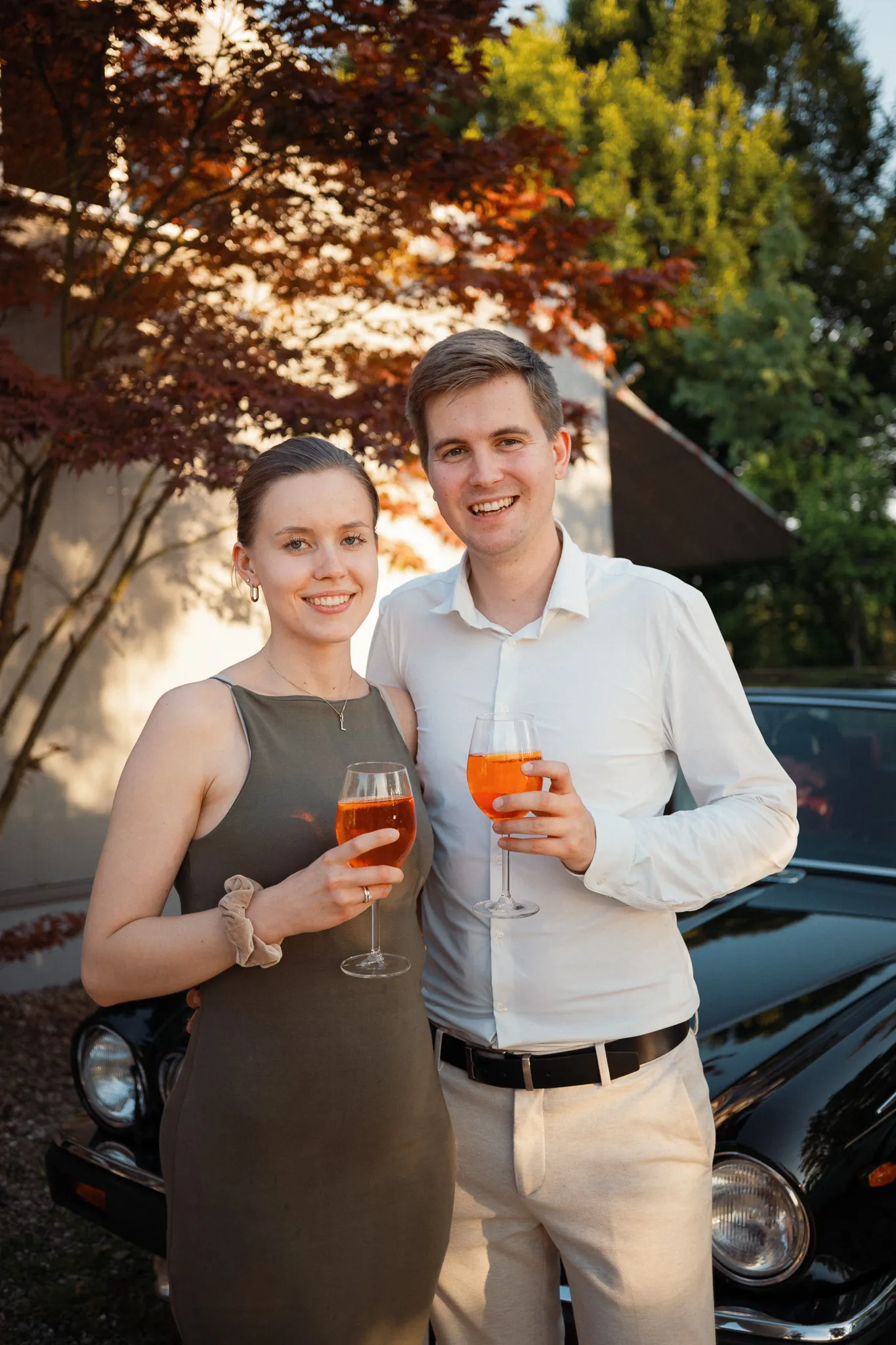 Zwei Hochzeitsgäste stehen mit orangefarbenen Getränken im Abendlicht.