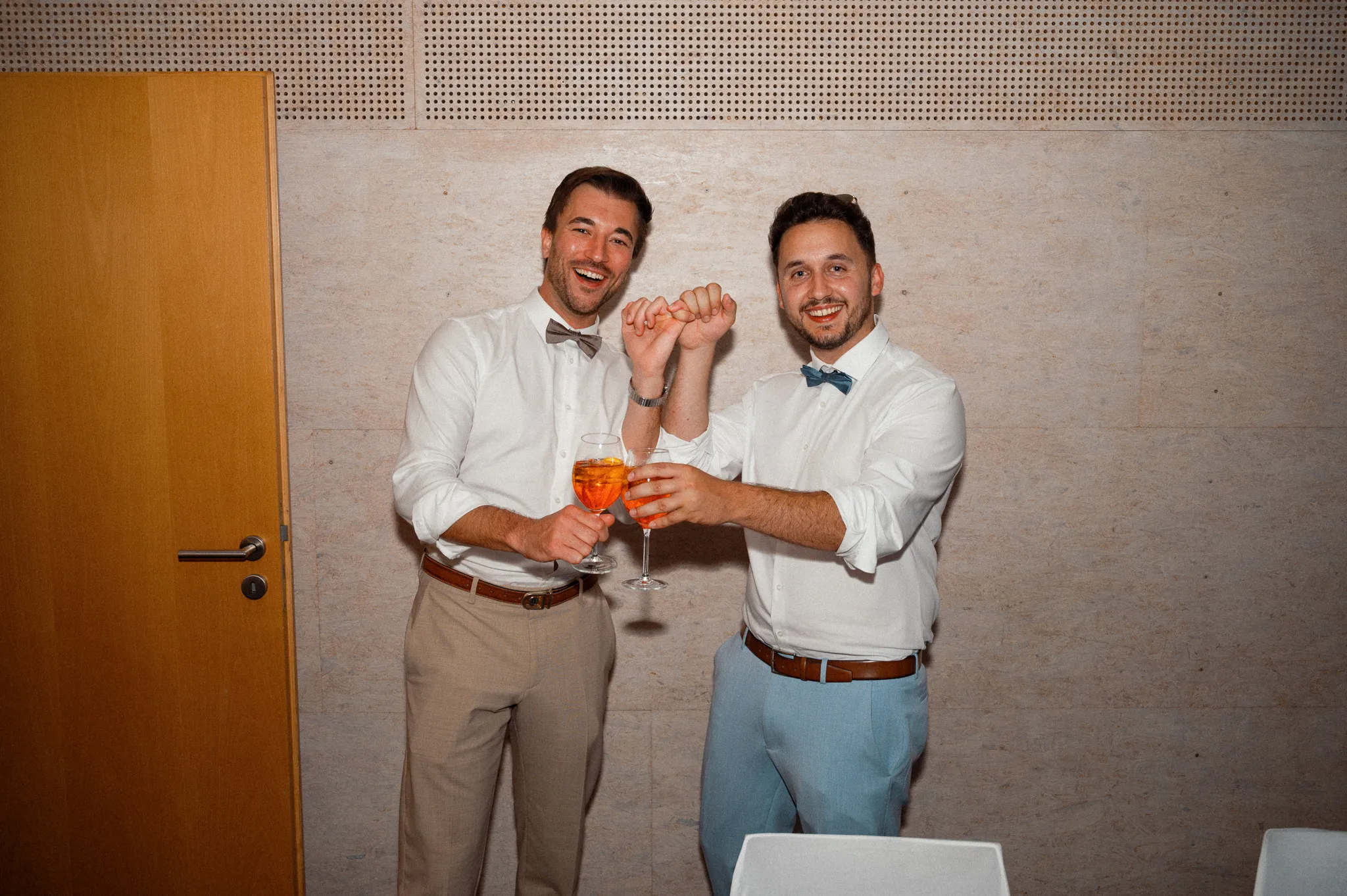 Zwei Gäste stoßen im Festsaal mit orangefarbenen Getränken an.
