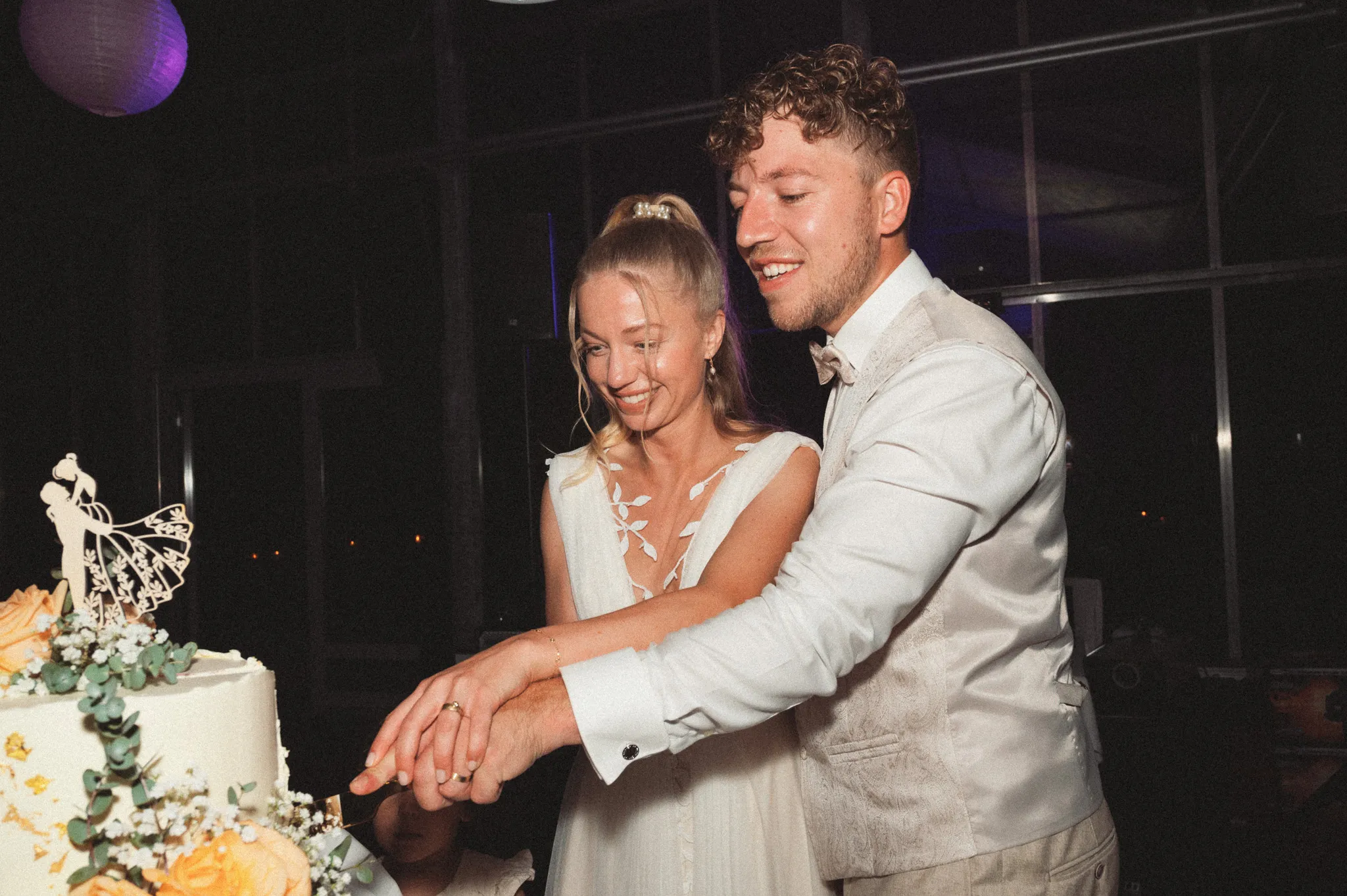 Franziska und Daniel lachen beim Anschneiden der Hochzeitstorte.
