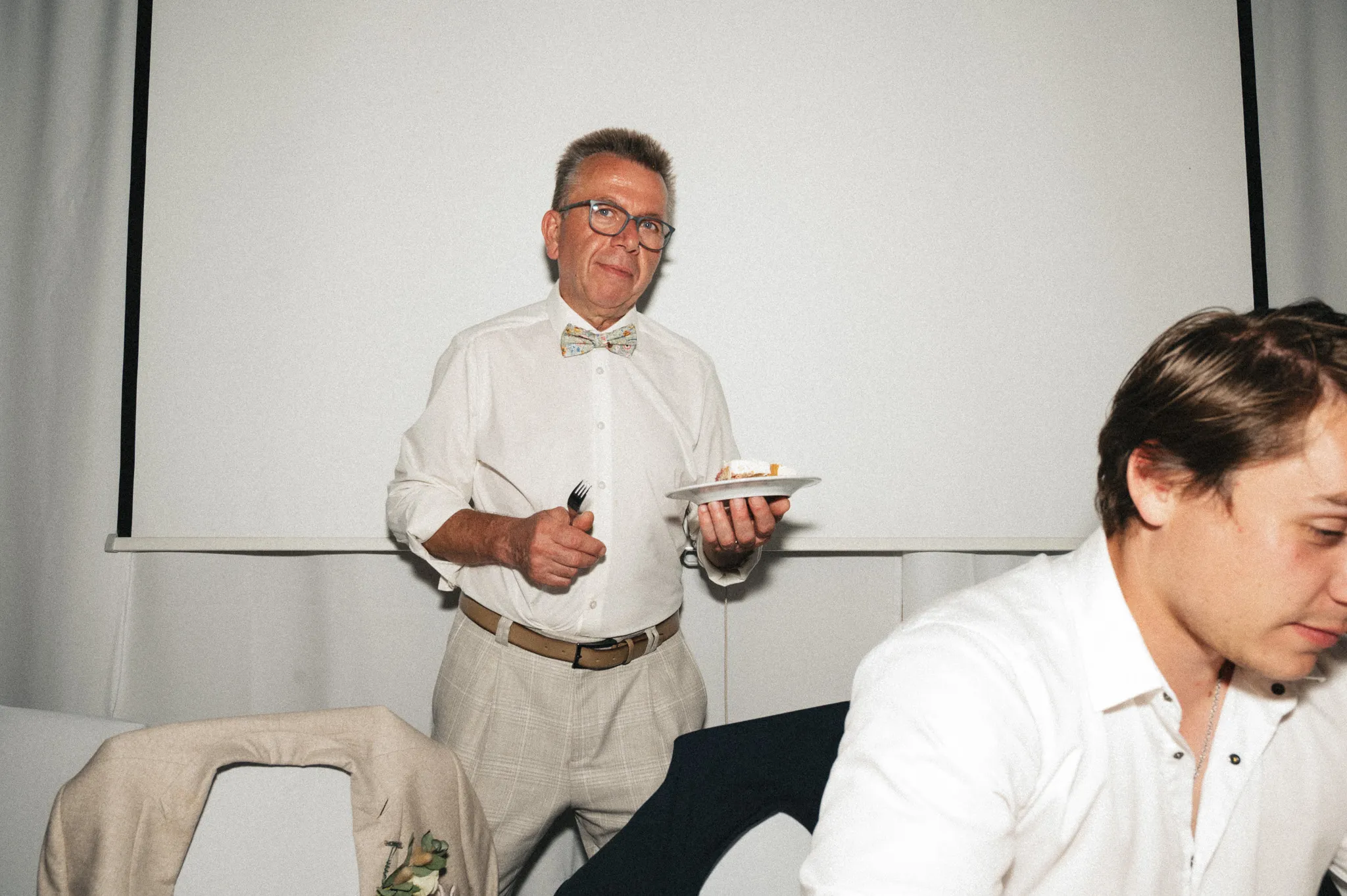 Ein Hochzeitsgast trägt einen Teller mit Torte durch den Festsaal.