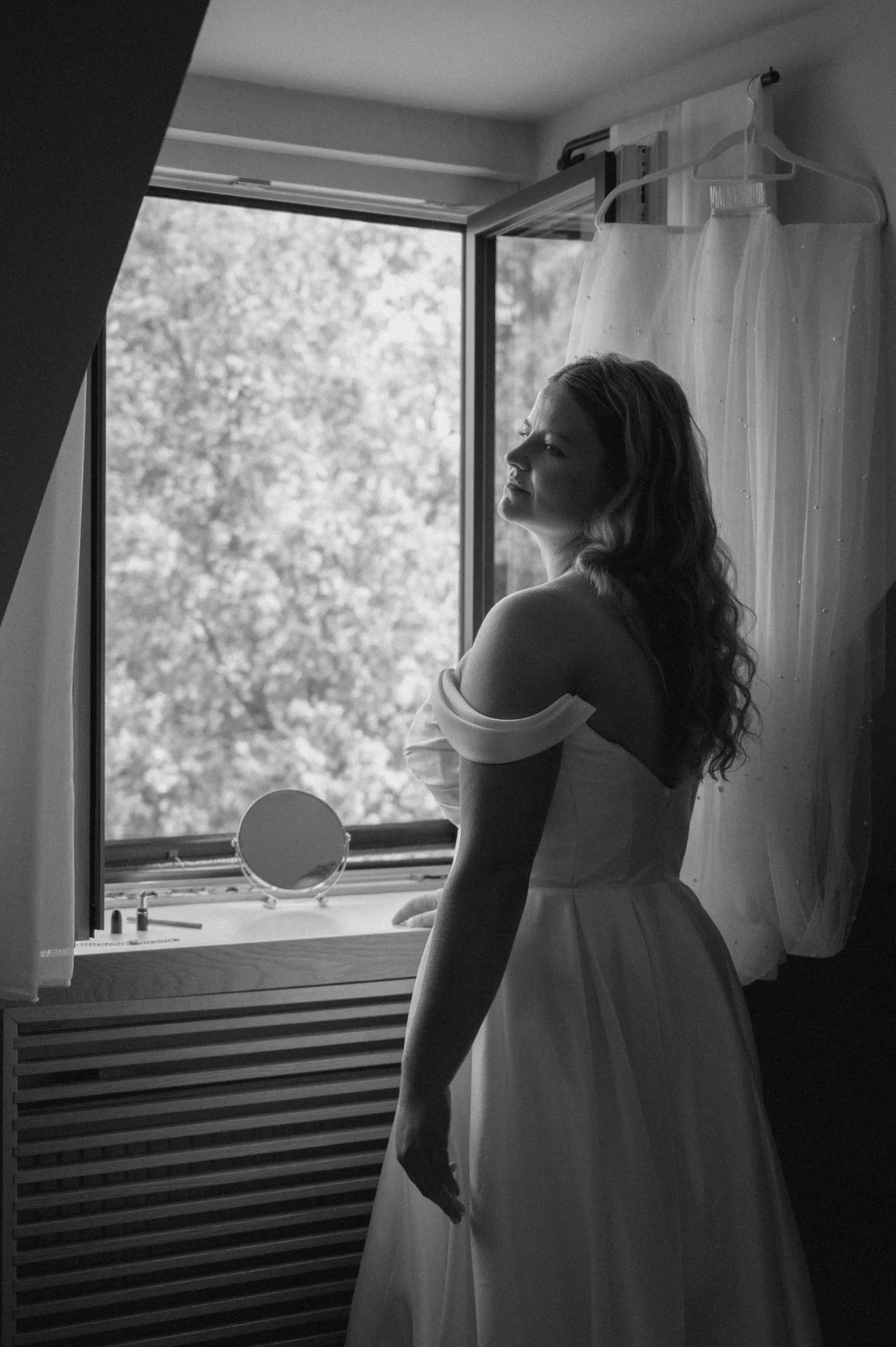 Lisa steht im Hochzeitskleid am Fenster und blickt nach draußen.