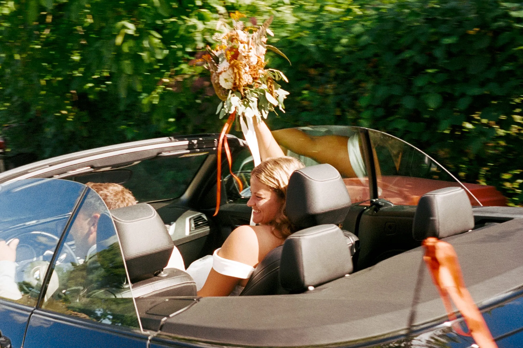 Lisa und Martin sitzen mit Blumen im offenen Auto.