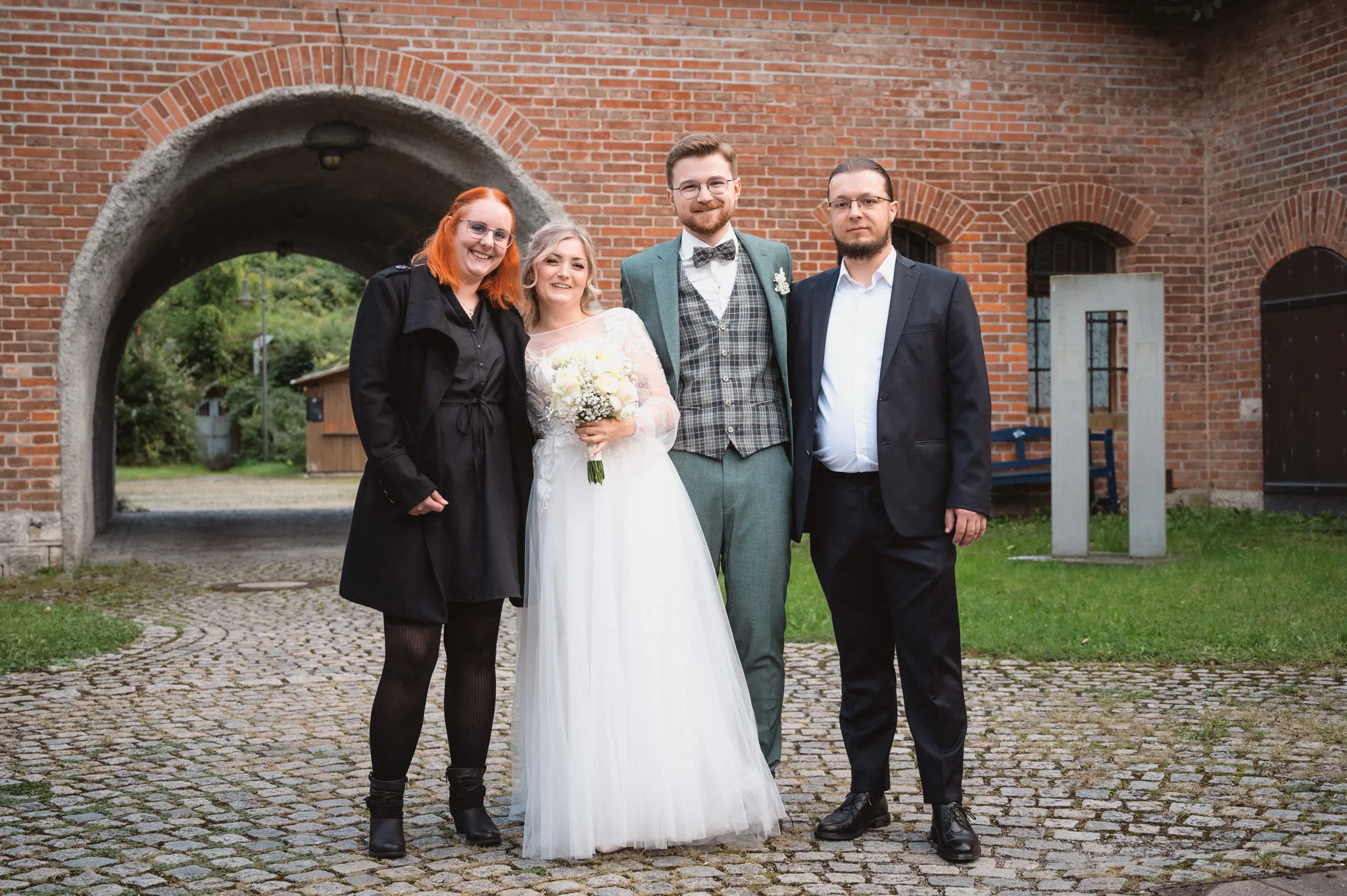 Tamara und Kevin stehen mit zwei Gästen im Innenhof des Backsteingebäudes.
