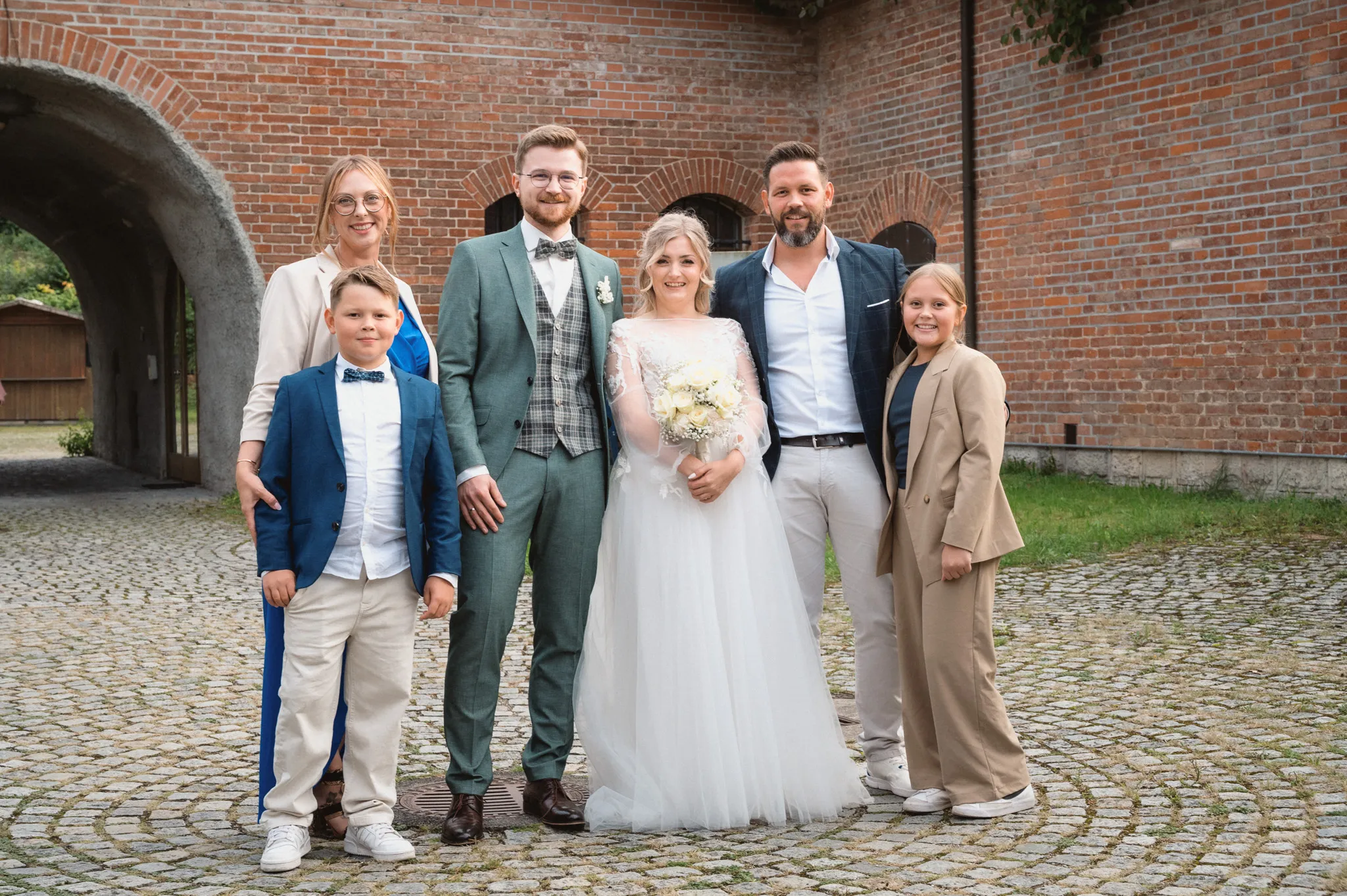 Tamara und Kevin stehen mit zwei jungen Gästen vor der Backsteinmauer.