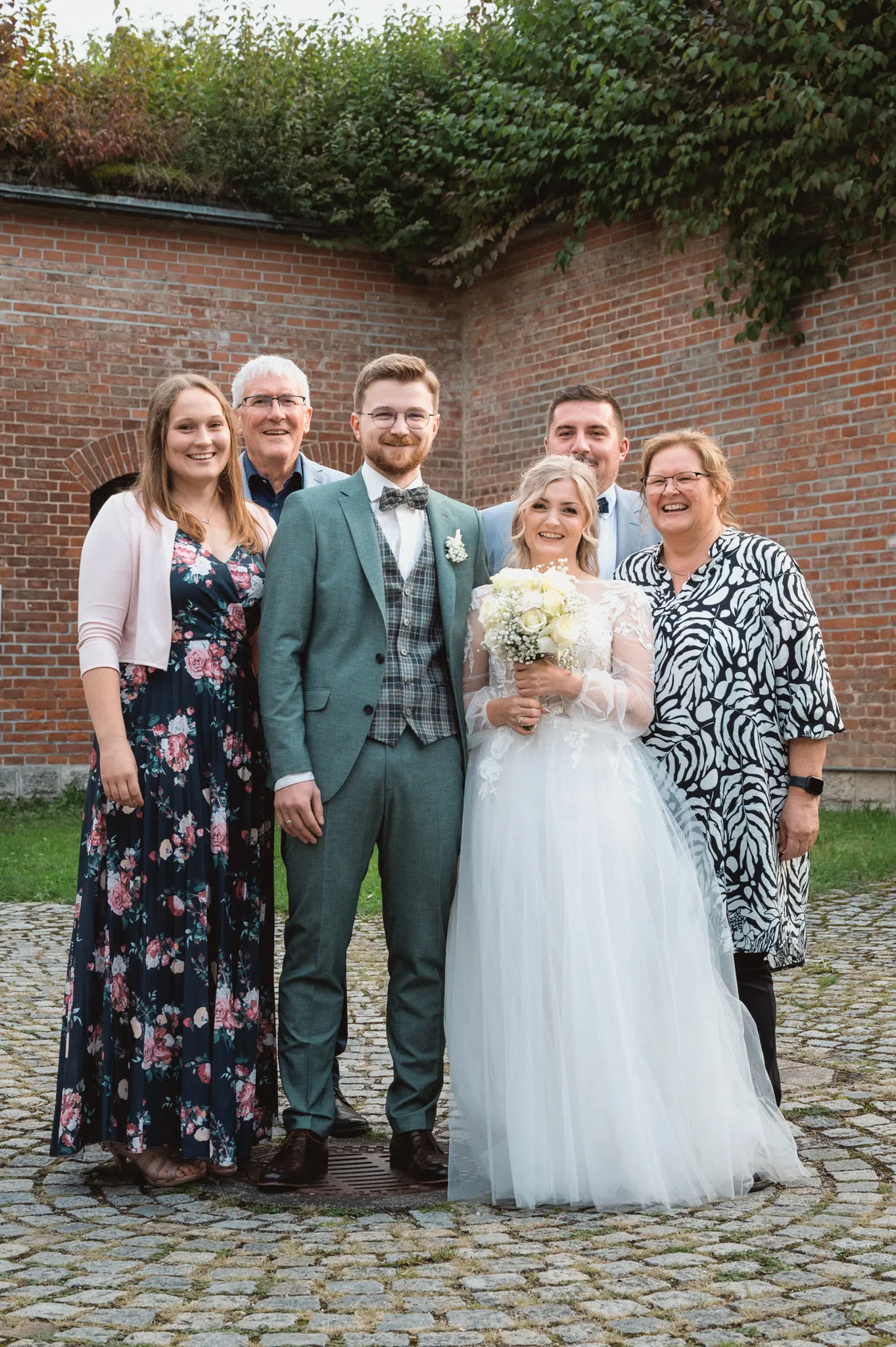 Tamara und Kevin stehen mit vier Gästen vor dem begrünten Backsteingebäude.