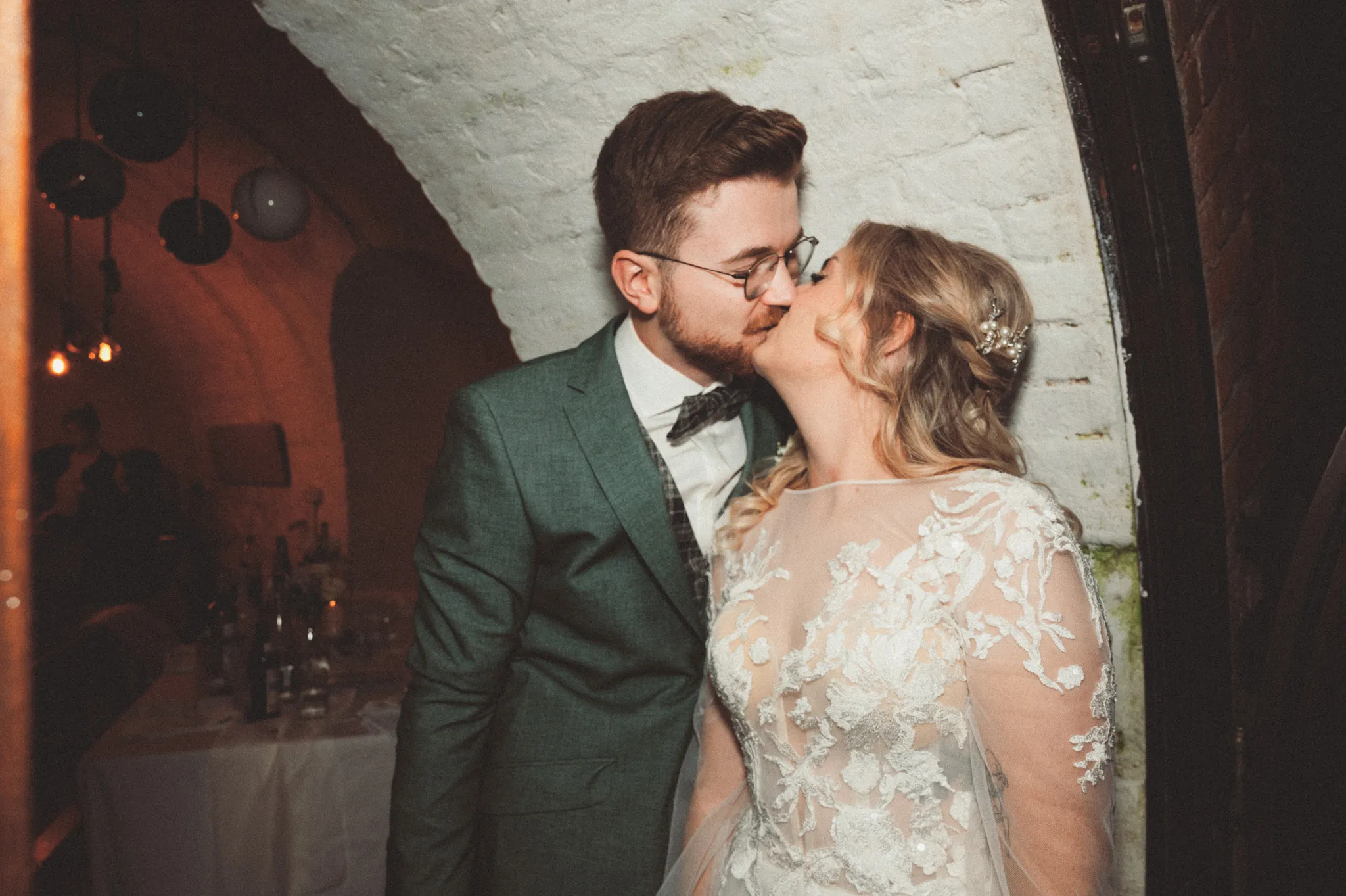 Tamara und Kevin küssen sich während der Feier vor einer hellen Backsteinwand.