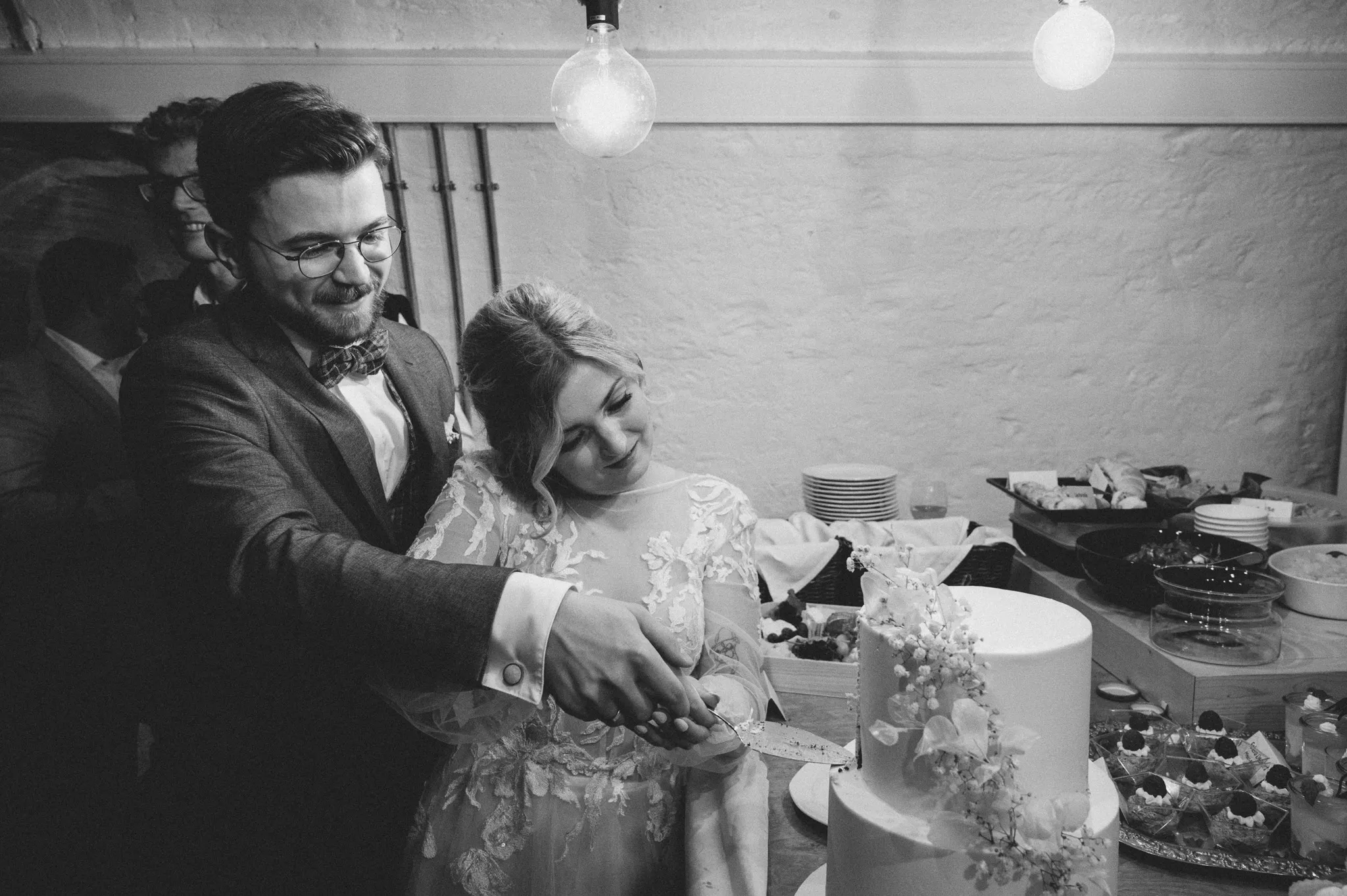 Tamara und Kevin lachen in einer Schwarz-Weiß-Aufnahme beim Anschneiden der Torte.