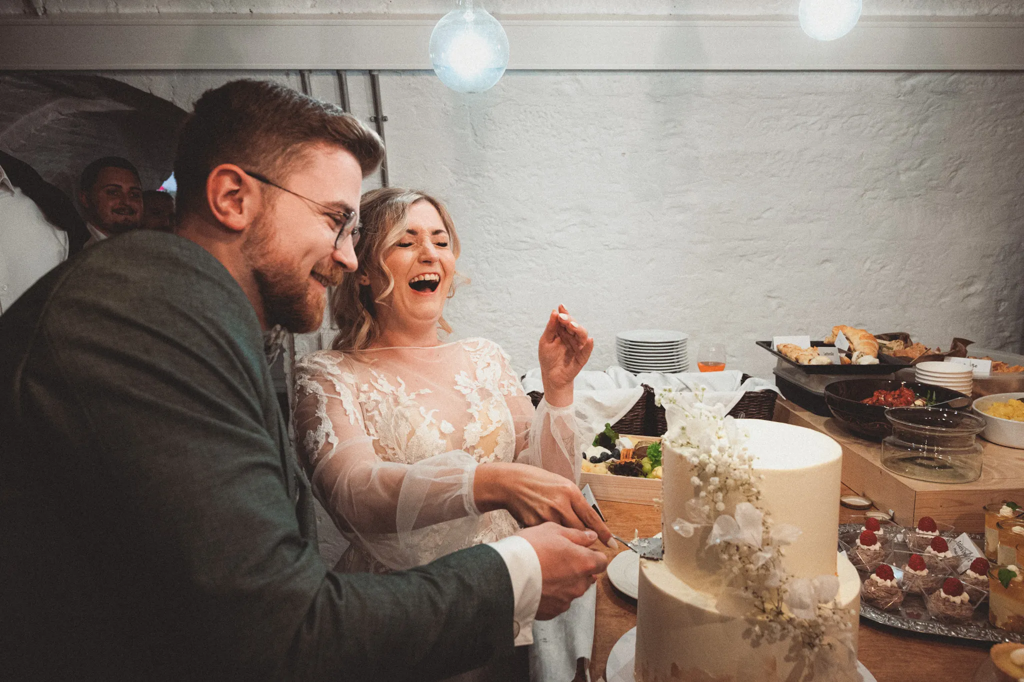Tamara und Kevin lachen miteinander am Tisch mit der angeschnittenen Hochzeitstorte.