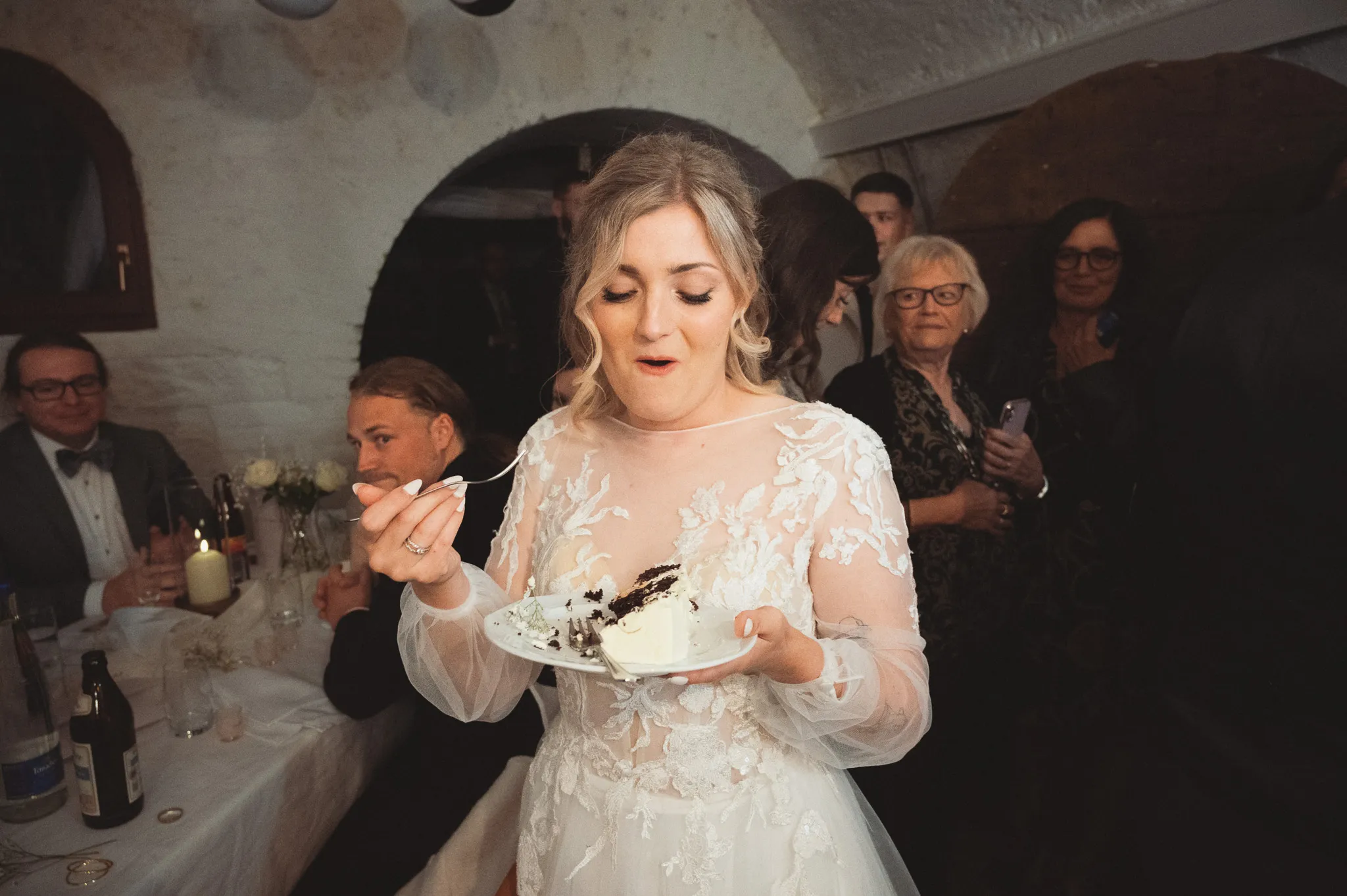 Tamara probiert ein Stück Hochzeitstorte, während die Gäste hinter ihr zusehen.