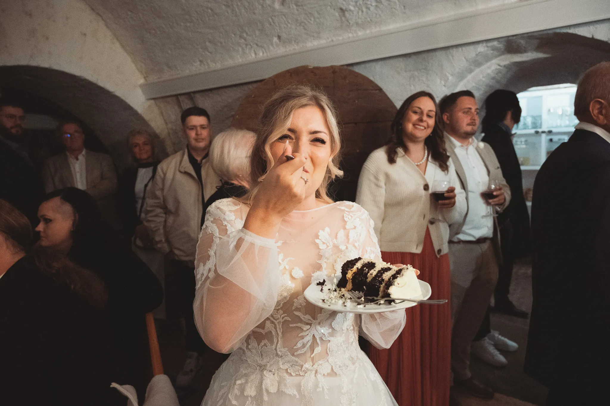 Tamara lacht mit einem Teller Hochzeitstorte inmitten der Gäste.